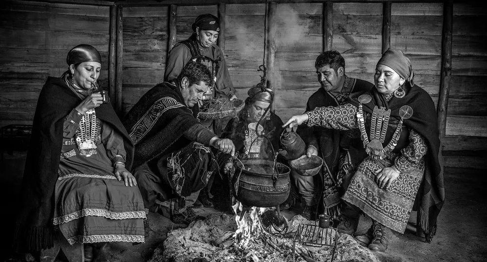 Grupo de personas mapuche reunidas en el interior de una ruka, en blanco y negro