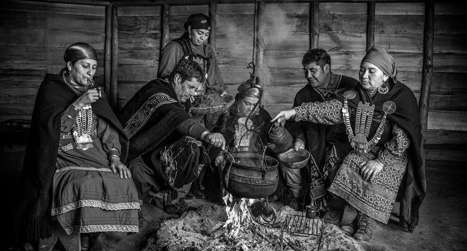 Grupo de personas mapuche reunidas en el interior de una ruka, en blanco y negro