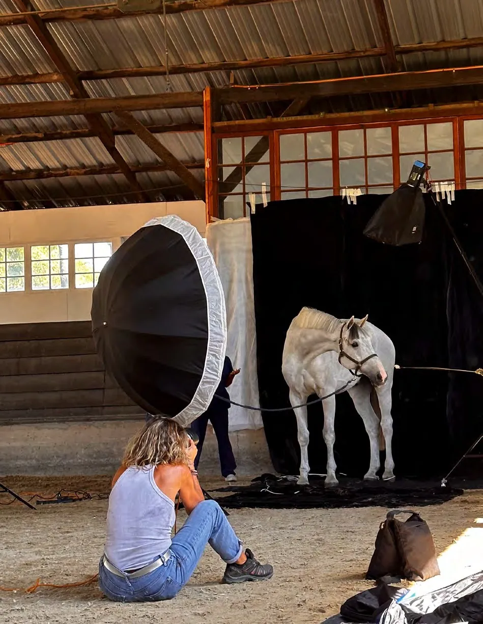 Gloria Franke sentada frente a un caballo blanco, entre focos y un paraguas de iluminación, en un picadero