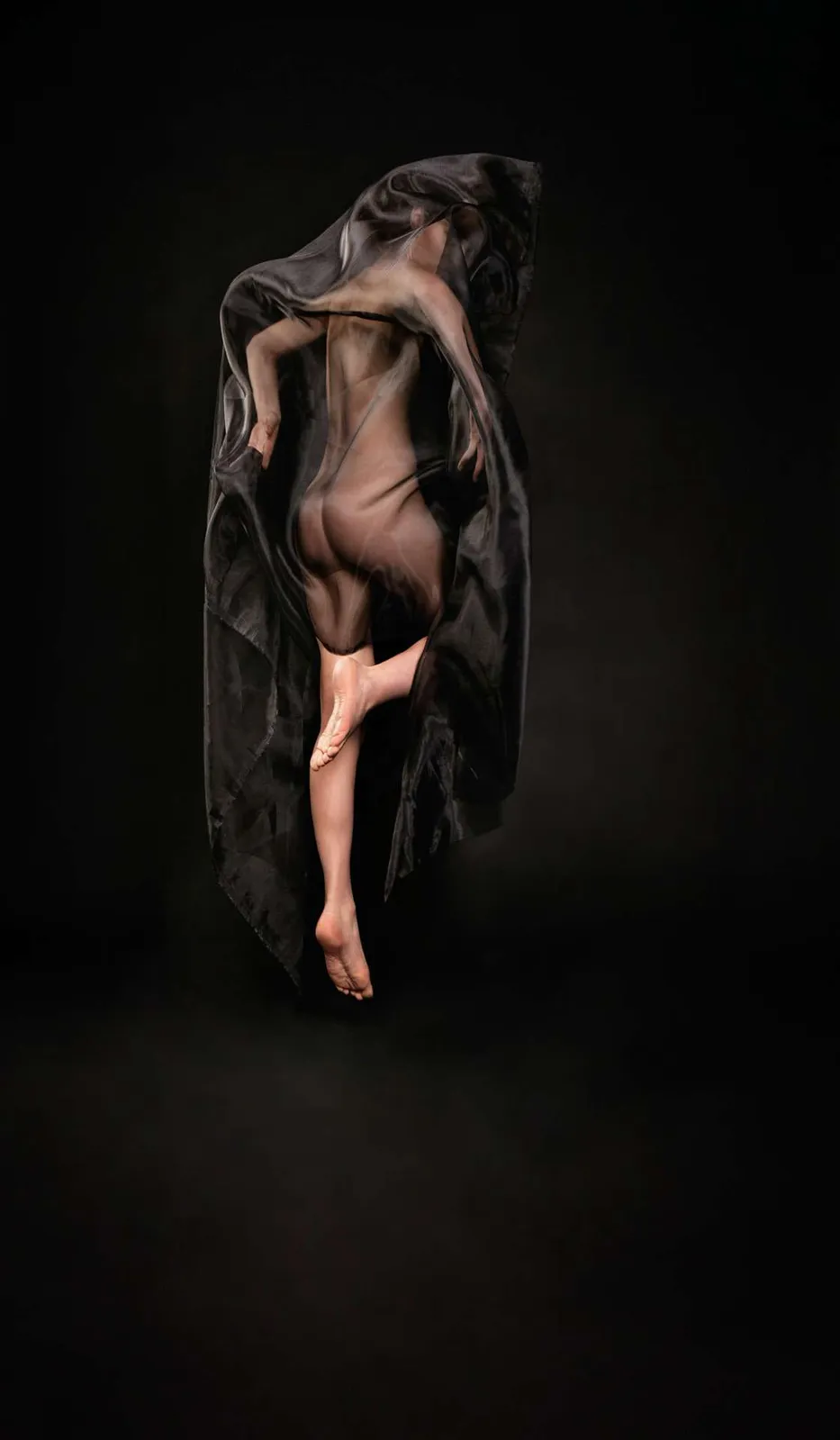Modelo de espaldas cubierta por una tela transparente oscura, sobre fondo negro