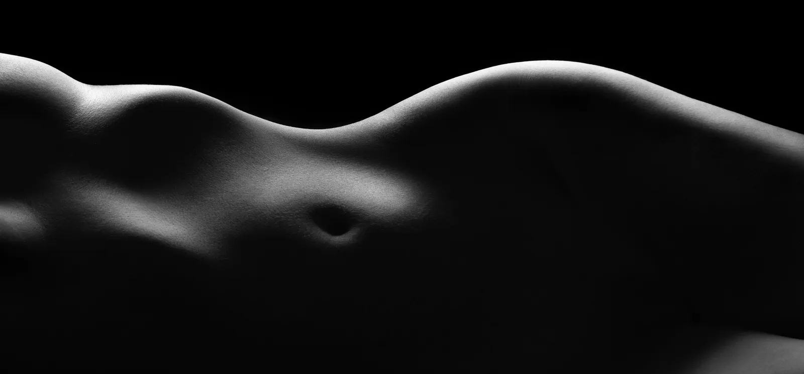 Silueta de un cuerpo que forma una curva como una duna, sobre fondo negro