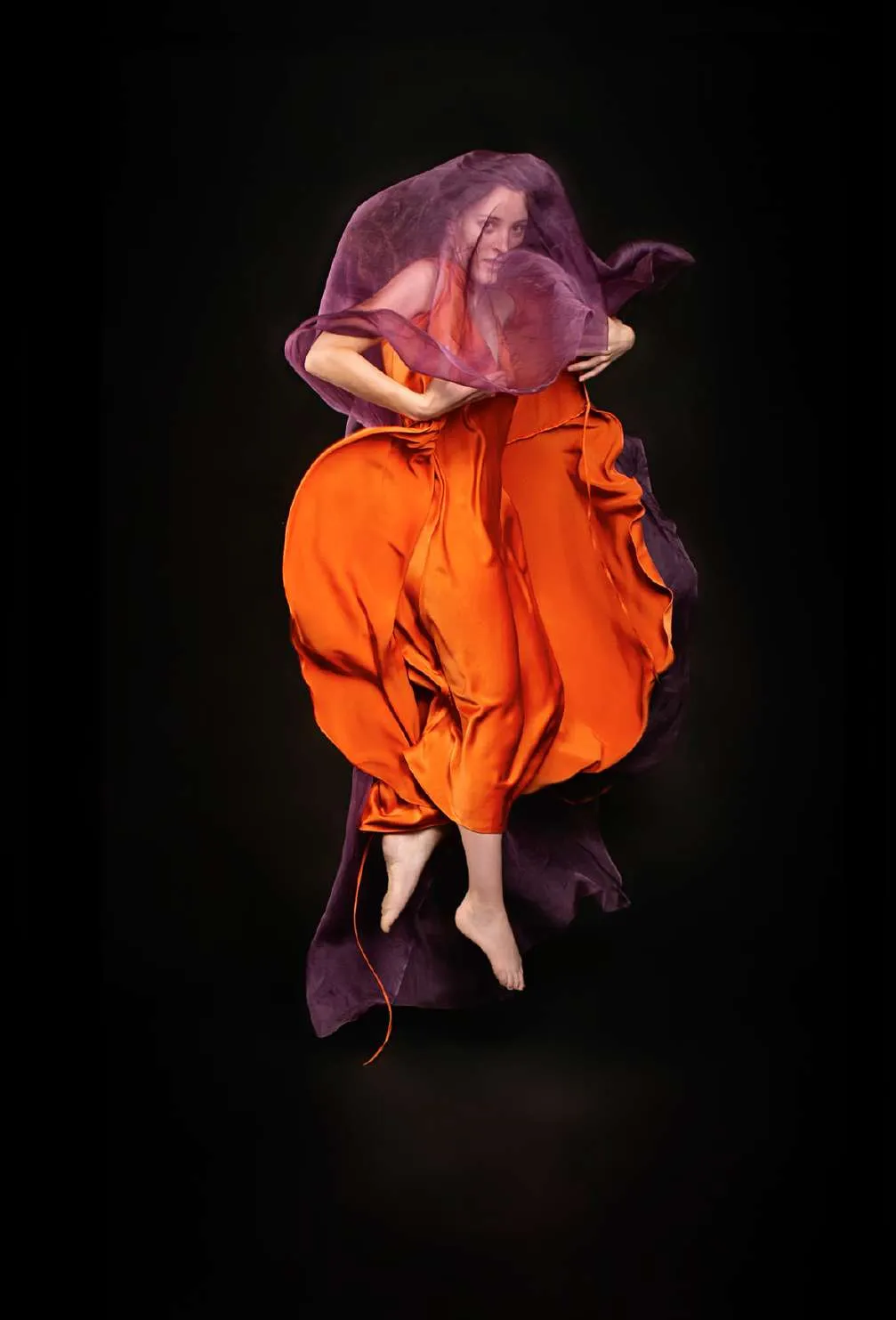 Modelo en el aire con un vestido naranja y una tela violeta, sobre fondo negro