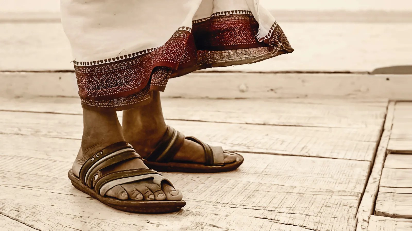Pies con sandalias y un pantalón de borde bordado sobre tablas de madera