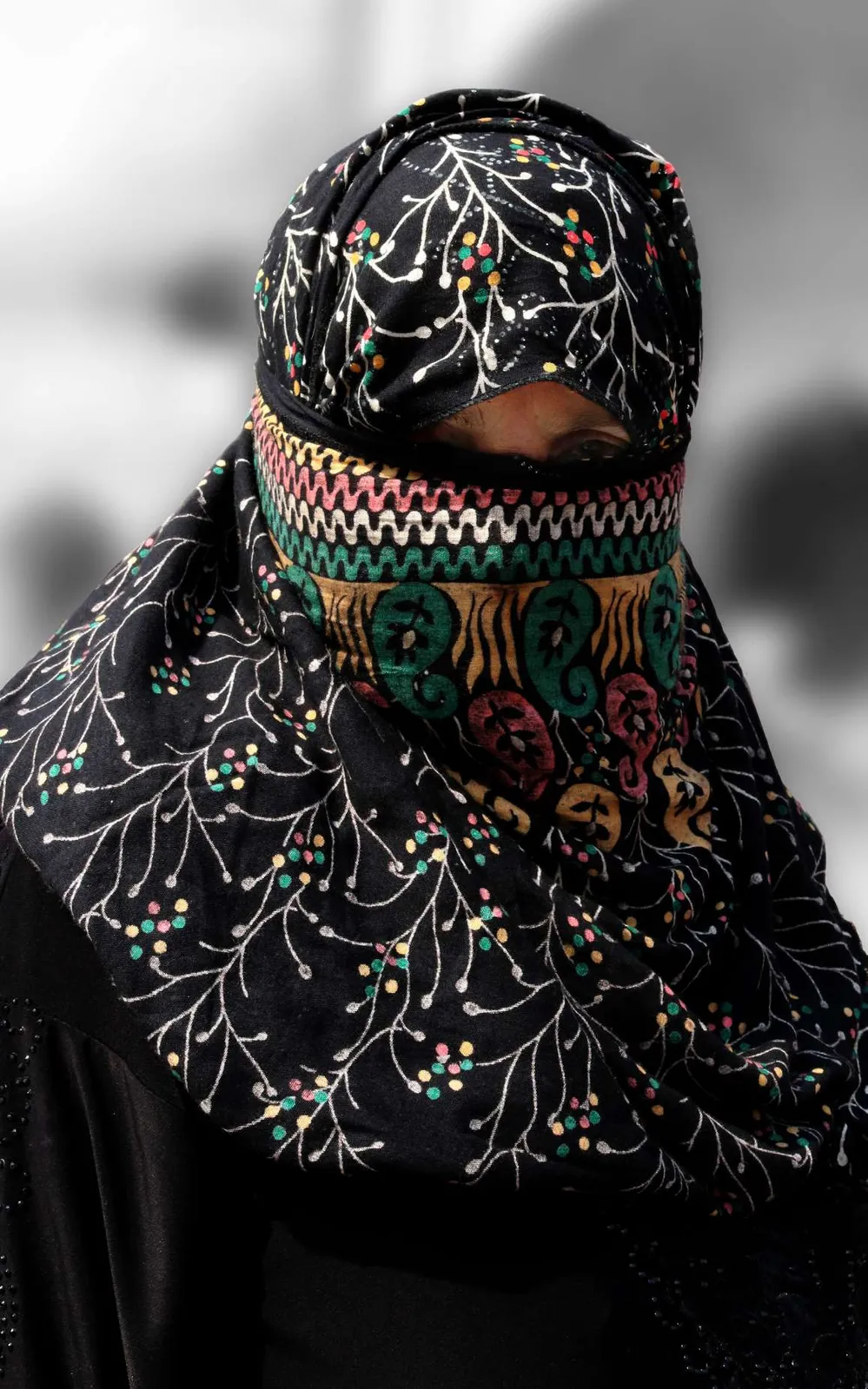Persona con el rostro cubierto por un velo negro bordado de colores
