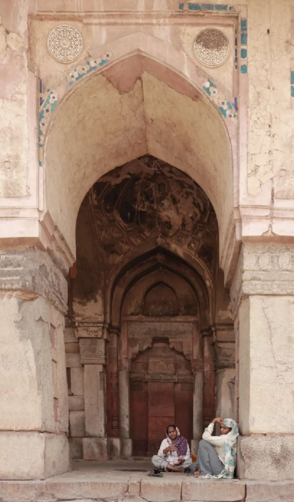 Dos personas sentadas en el umbral de un gran arco de piedra tallada