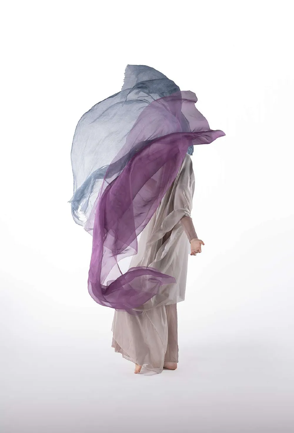 Modelo cubierta por telas violeta y celeste en movimiento, sobre fondo blanco