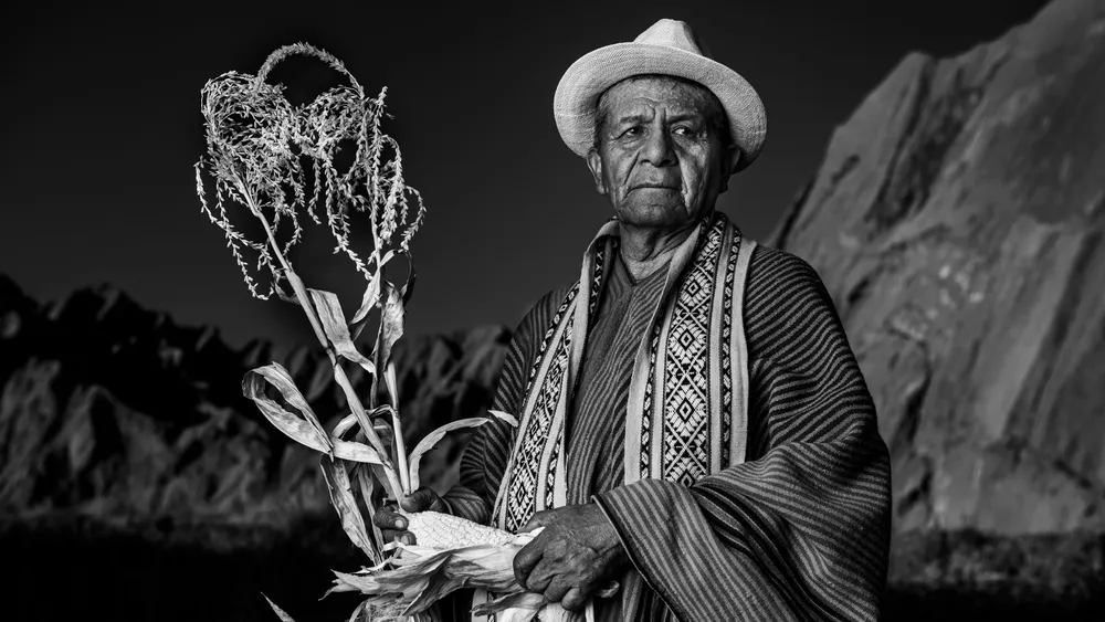 Hombre aymara con sombrero sosteniendo una planta, en blanco y negro