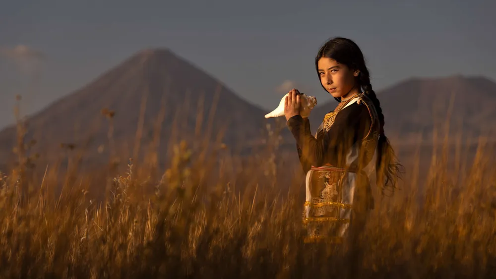 Mujer en un pastizal con un volcán al fondo