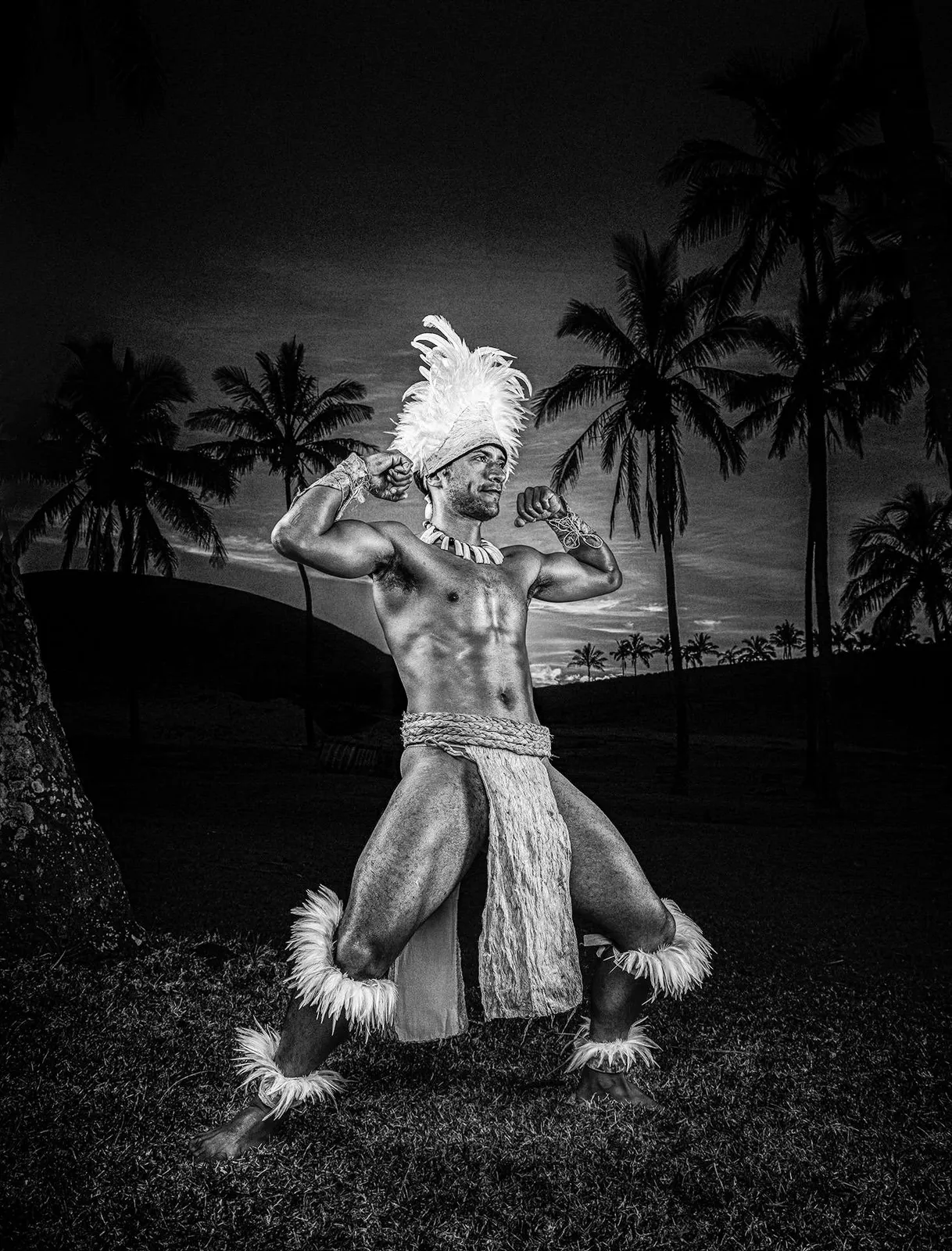 Figura rapa nui con un tocado de plumas sobre fondo oscuro, en blanco y negro