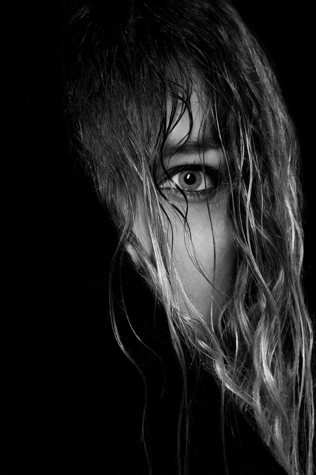 Mujer con el pelo sobre el rostro que deja ver un ojo, en blanco y negro