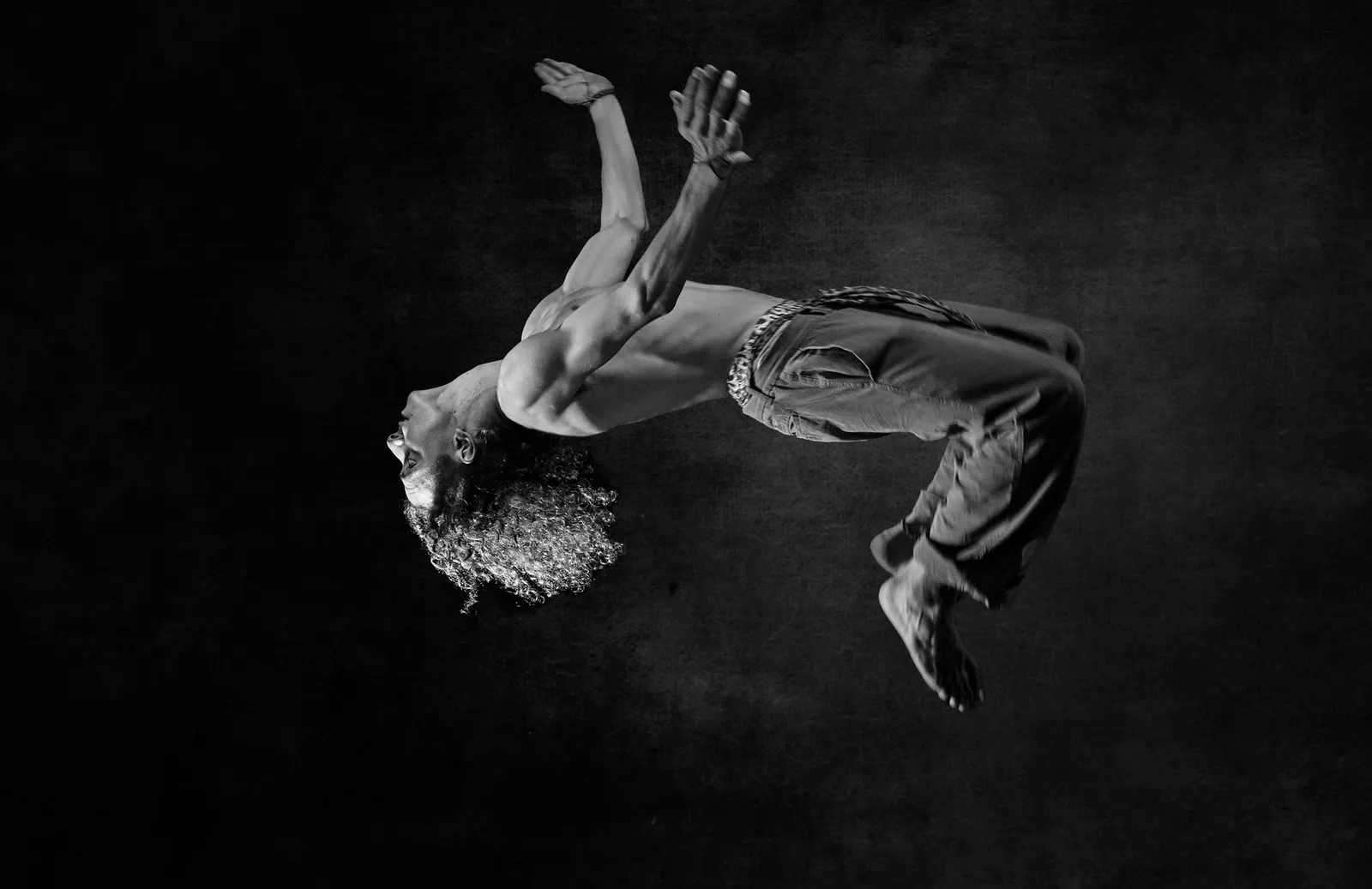 Cuerpo suspendido en el aire sobre fondo oscuro, en blanco y negro