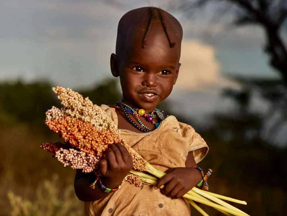 Niña hamer sosteniendo un ramo de sorgo