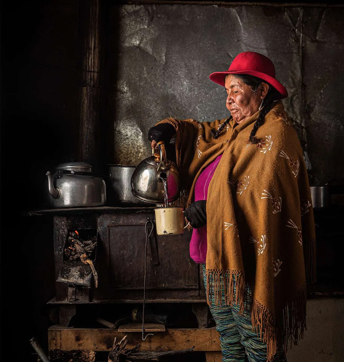 Mujer aymara con sombrero rojo junto a una cocina a leña