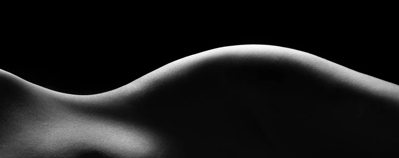 Silueta de un cuerpo recostado, iluminado de lado sobre fondo negro