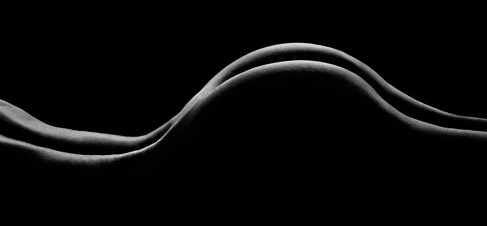 Curvas de un cuerpo iluminadas de lado sobre fondo negro