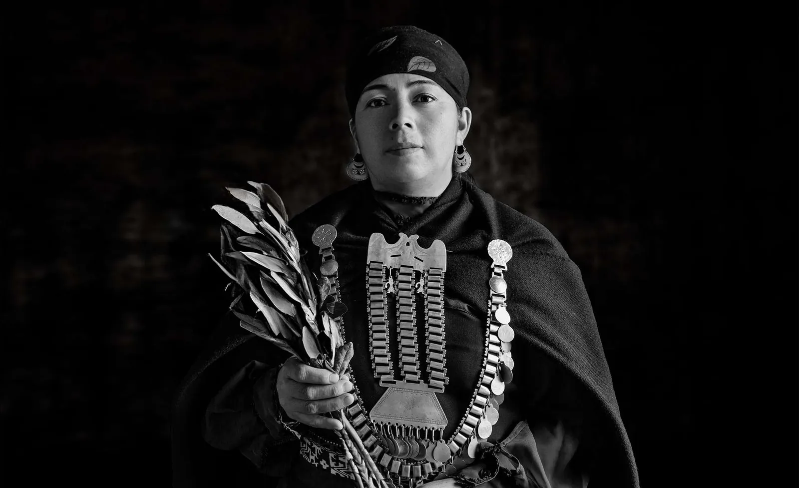 Mujer mapuche con joyas de plata y una rama, en blanco y negro